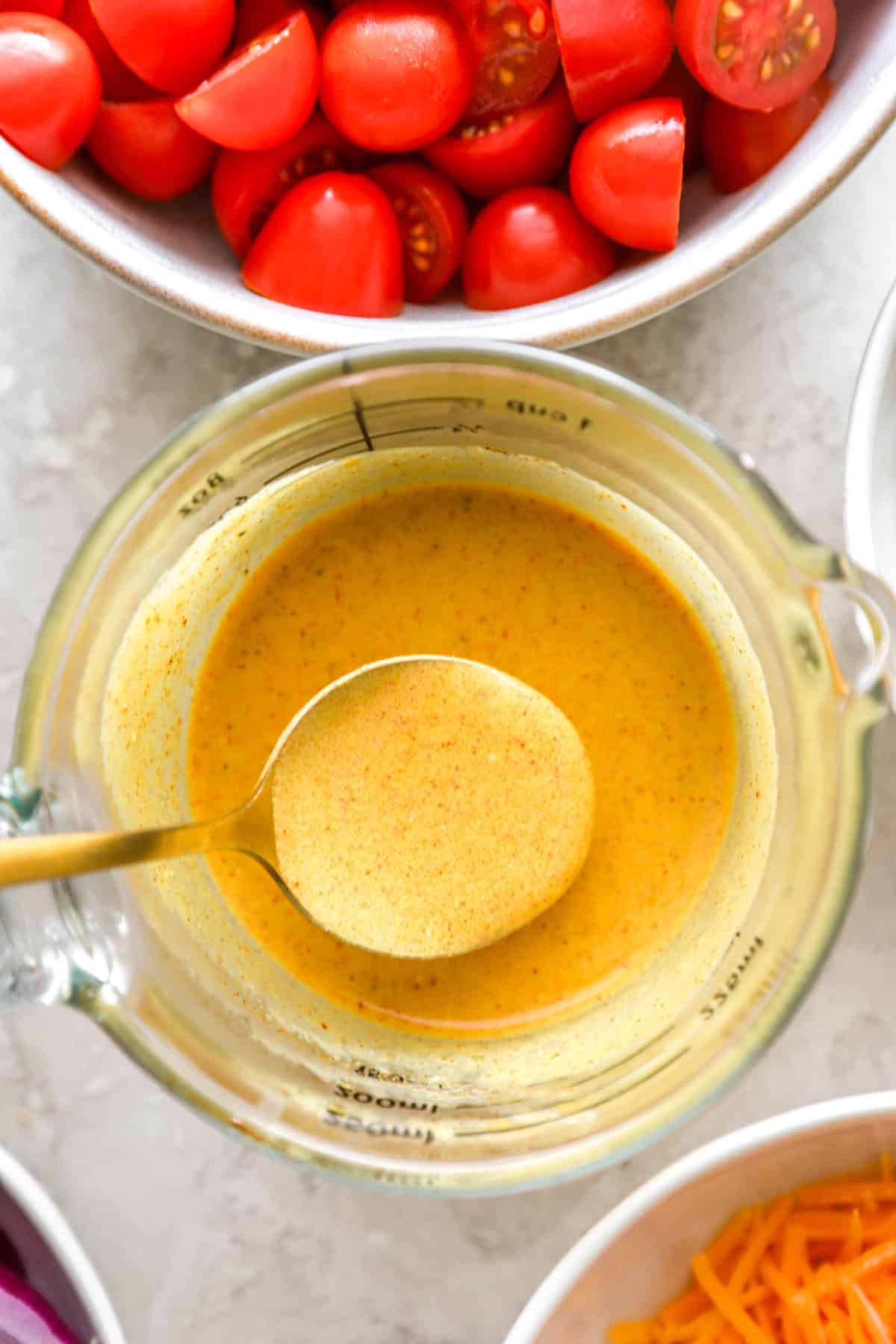 A spoon lifting a scoop of mustard dressing from a liquid measuring cup. 