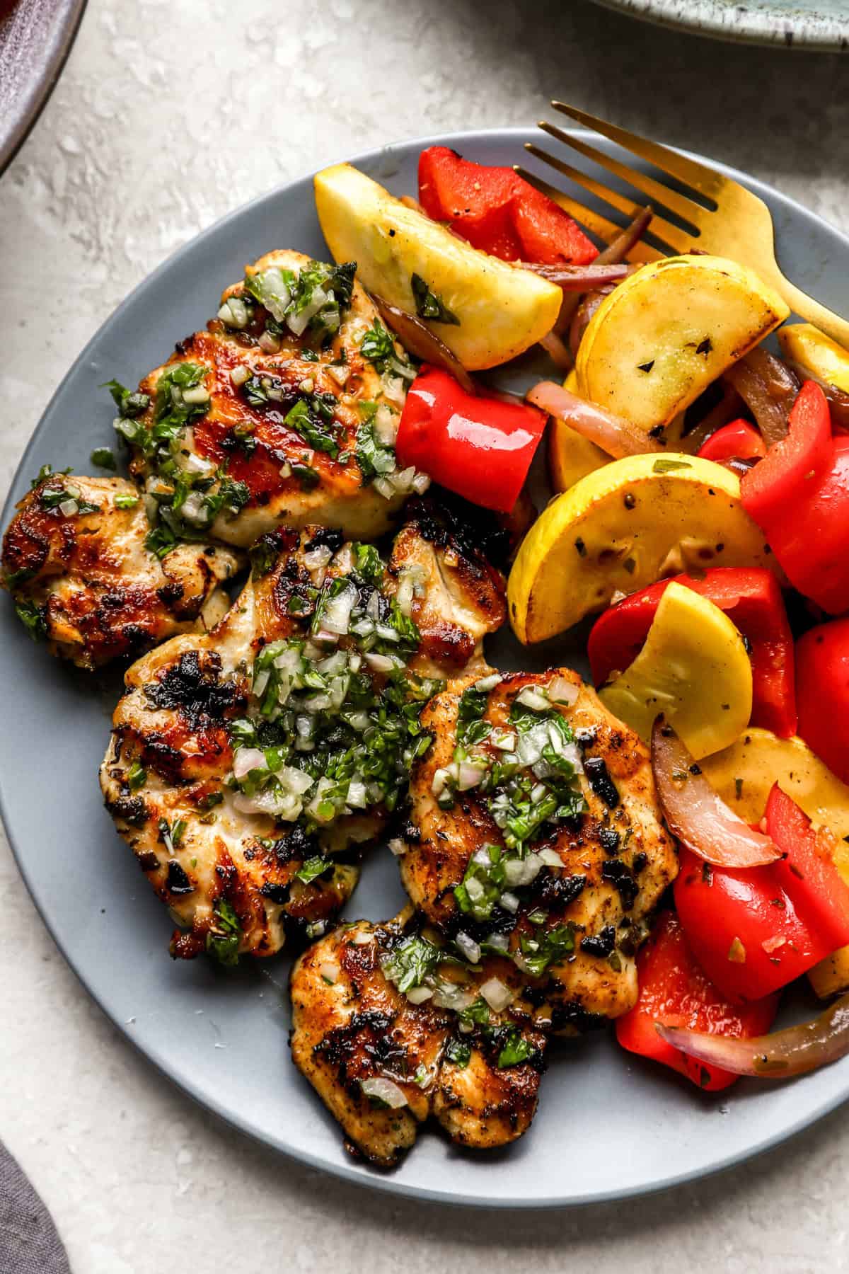 A plate of grilled chimichurri chicken and summer vegetables.