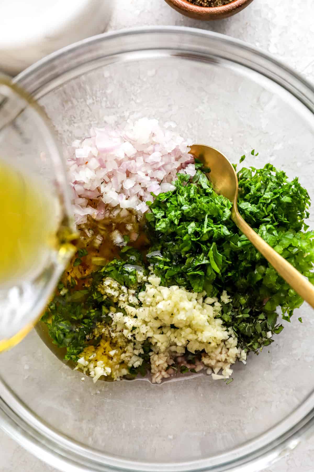 Olive oil being poured into a glass bowl to make chimichurri sauce.