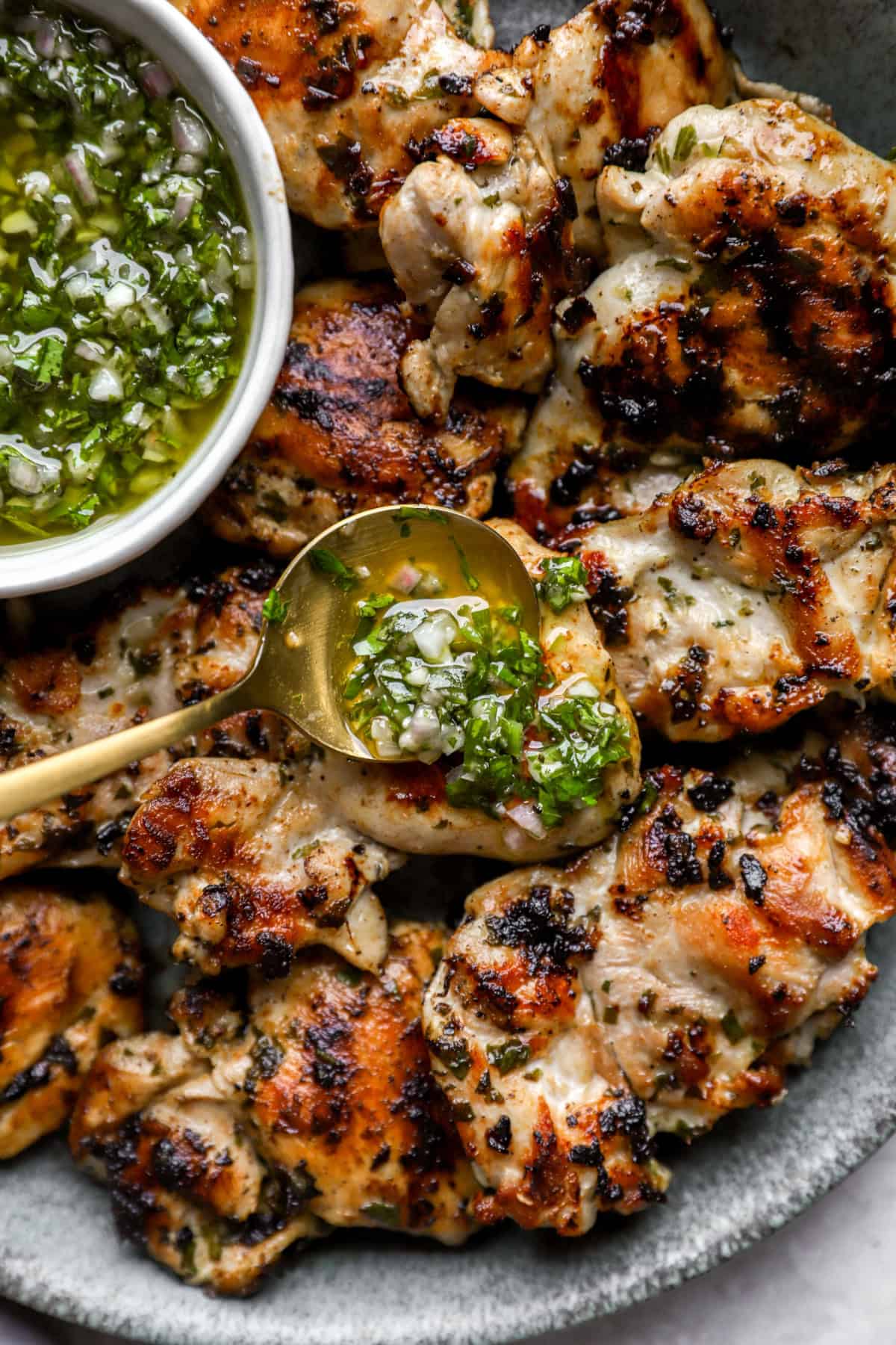 Chimichurri sauce being poured over grilled chicken. 