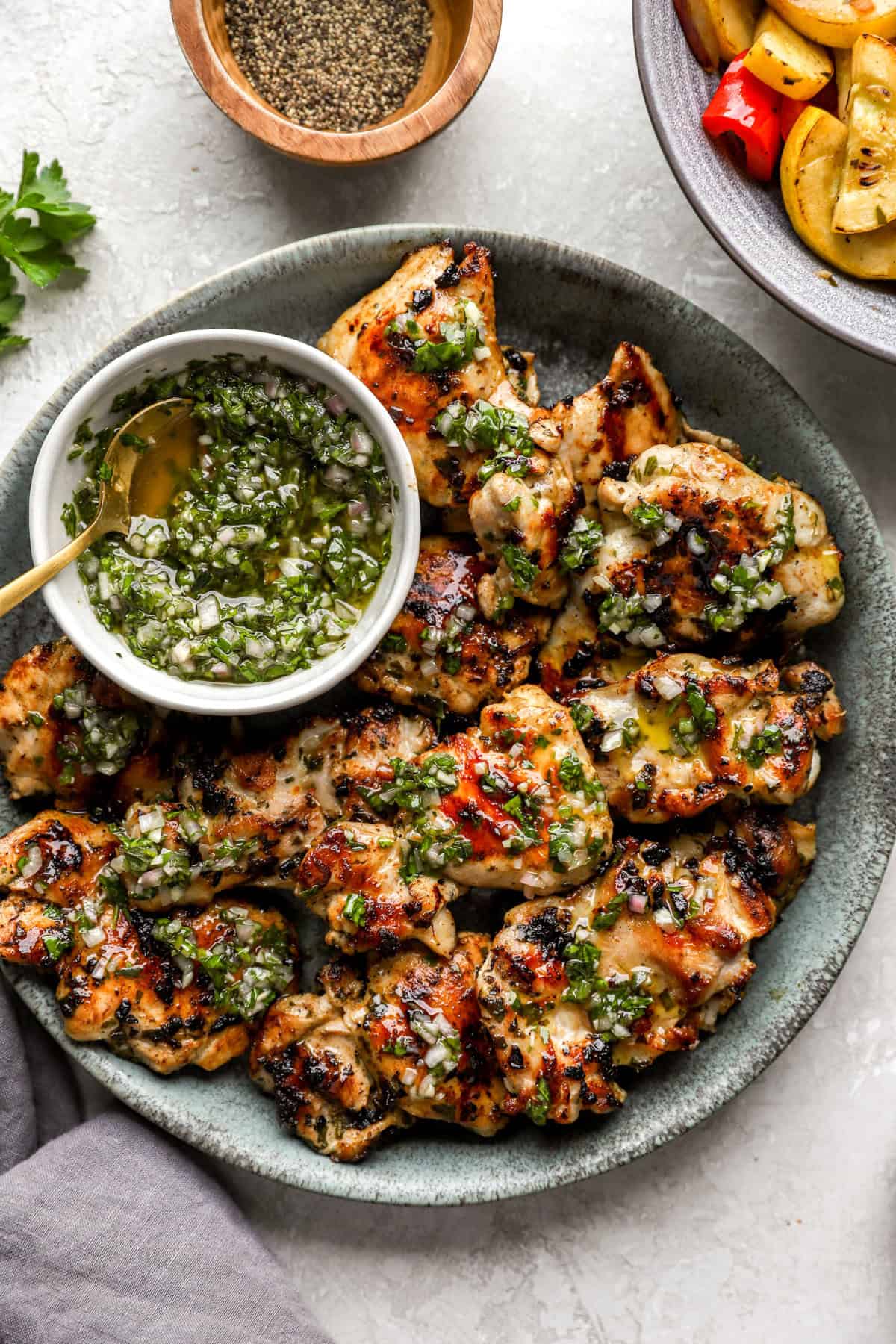 A plate of grilled chimichurri chicken with chimichurri on the side.