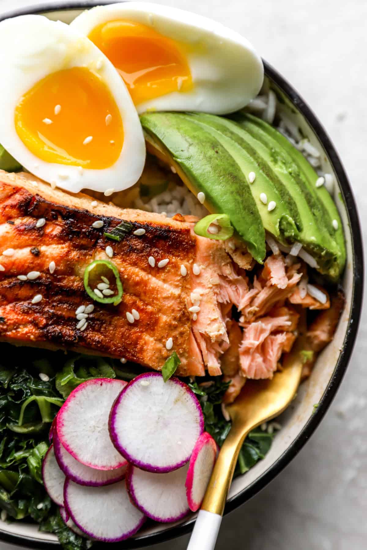 A grilled salmon bowl with a fork flaking a bite of salmon. 