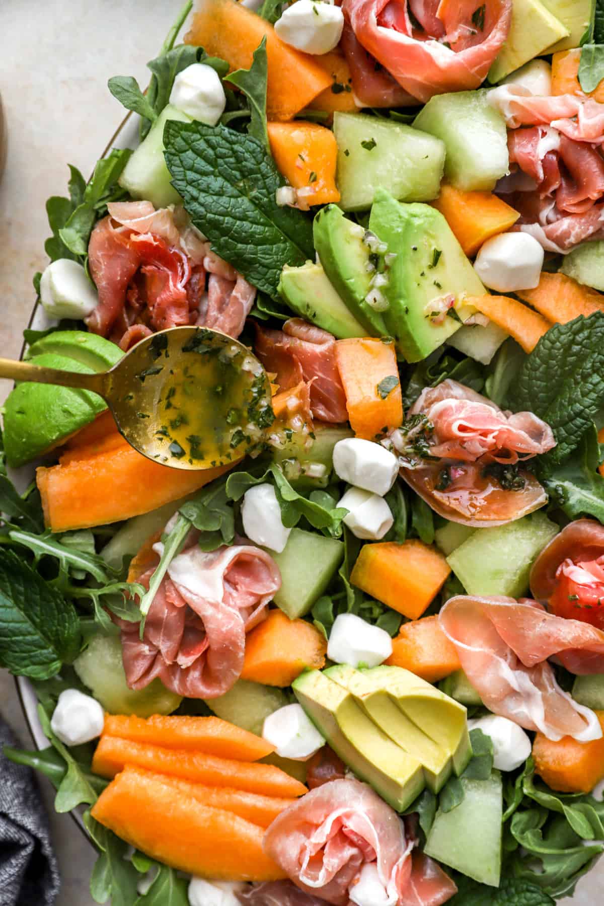 Dressing being drizzled over melon and prosciutto salad. 