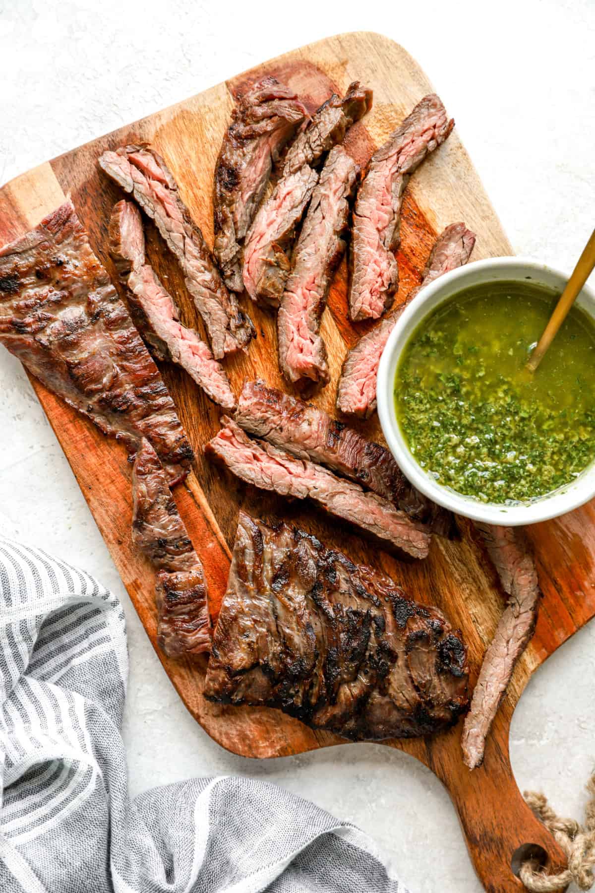 Sliced skirt steak pieces on a wooden cutting board next to a bowl of salsa verde. 