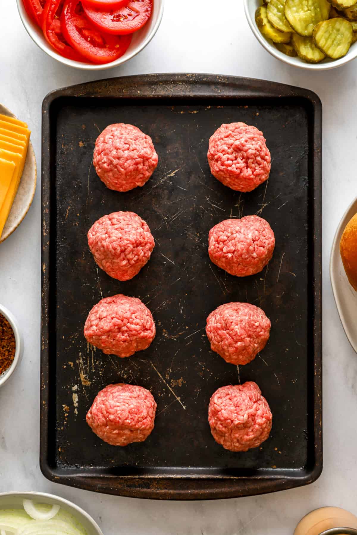 3 ounce ground beef patties on a baking sheet. 