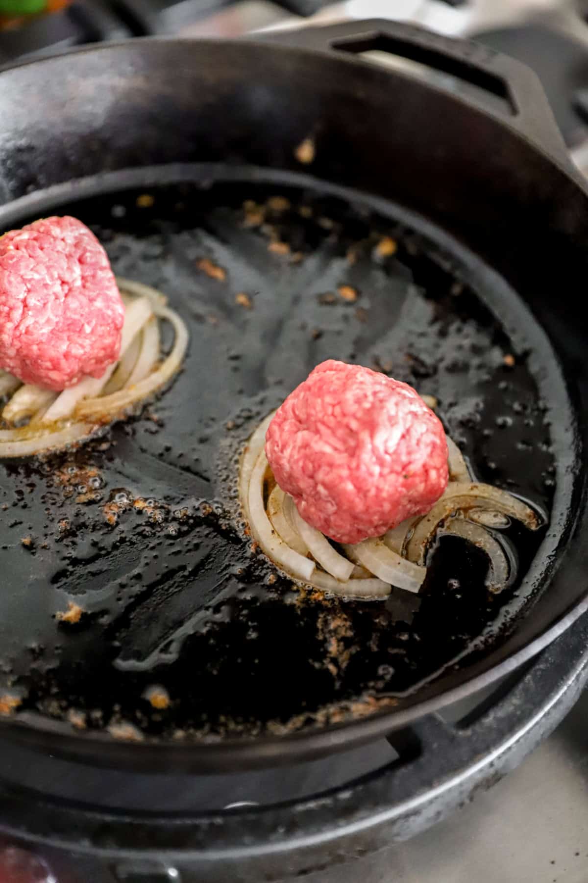 Burger patties on top of sautéed onions in a skillet.