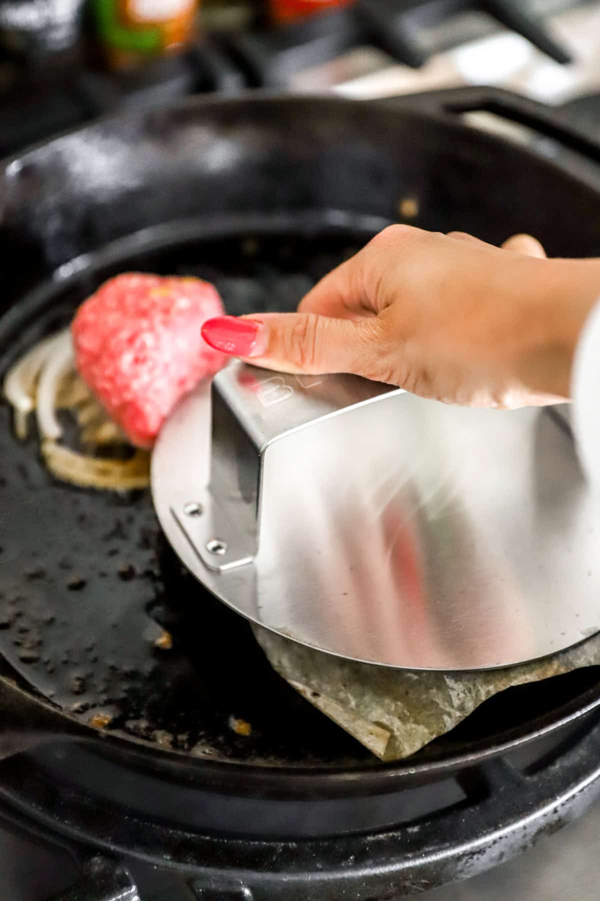 A hand using a burger press to create smash burgers in a skillet.