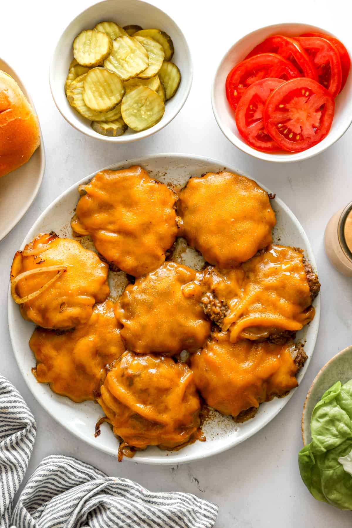 Homemade smash burgers on a plate surrounded by toppings. 