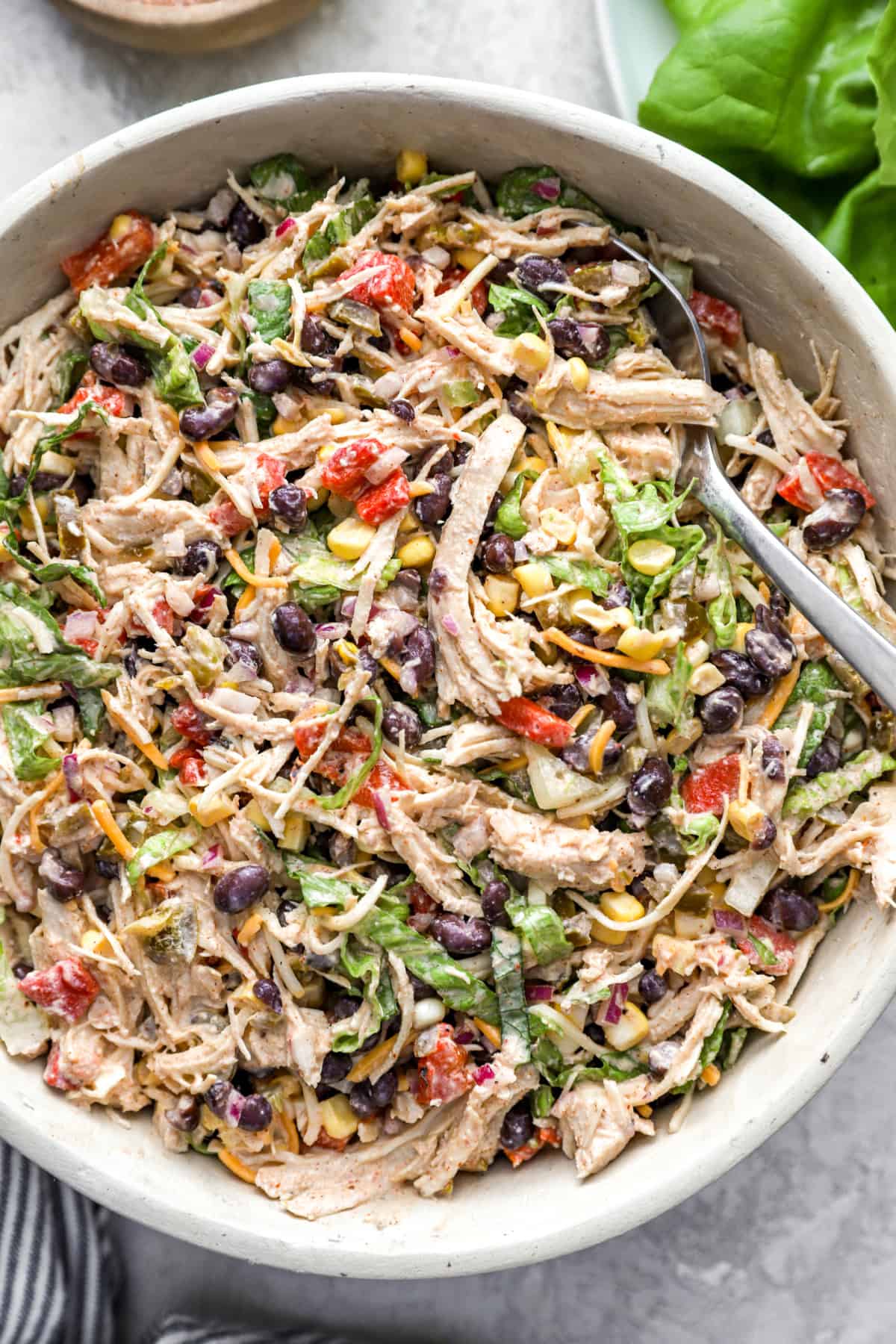 A bowl of chicken taco salad with tongs sticking out. 