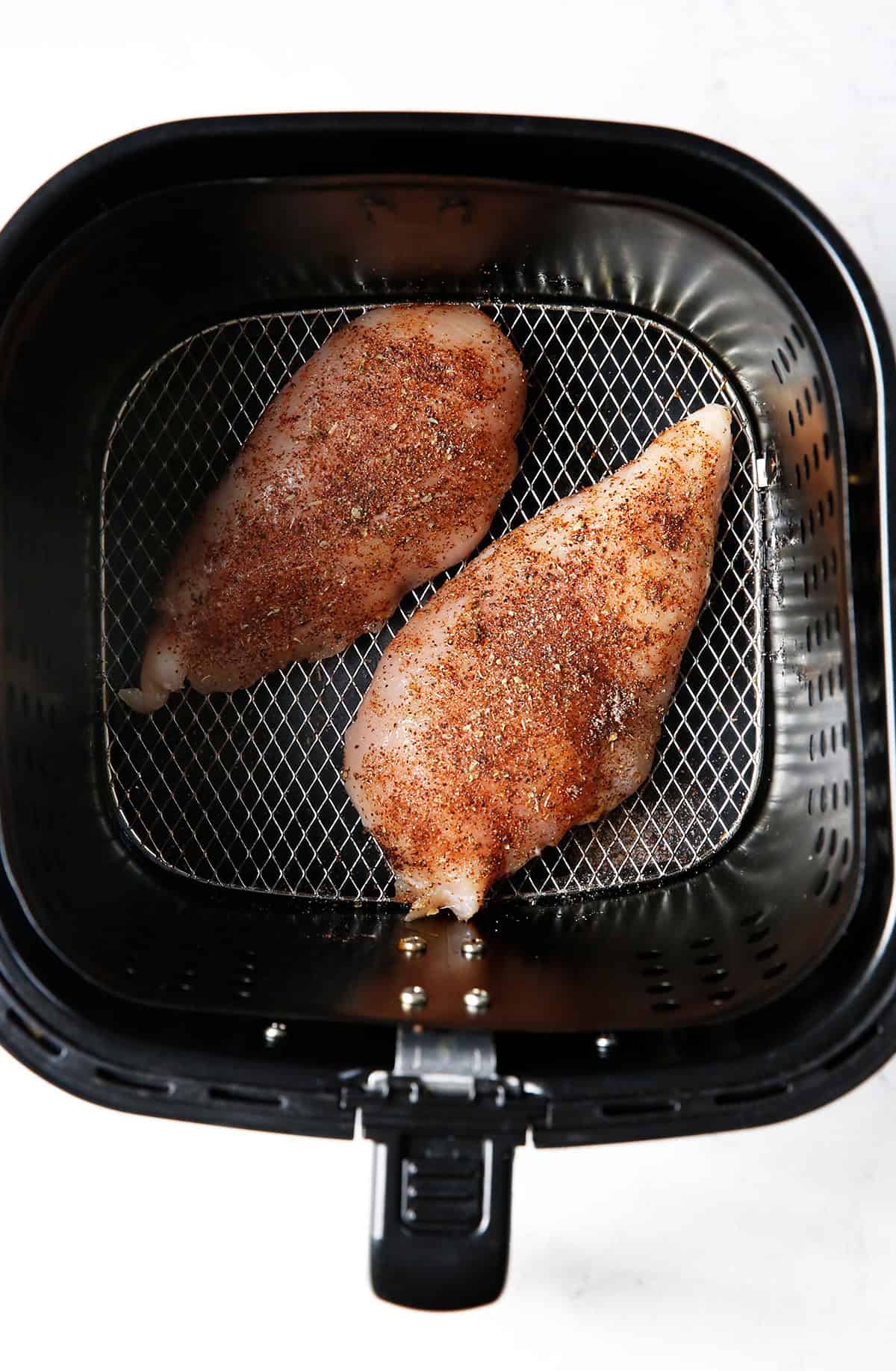 Raw seasoned chicken breasts in an air fryer. 