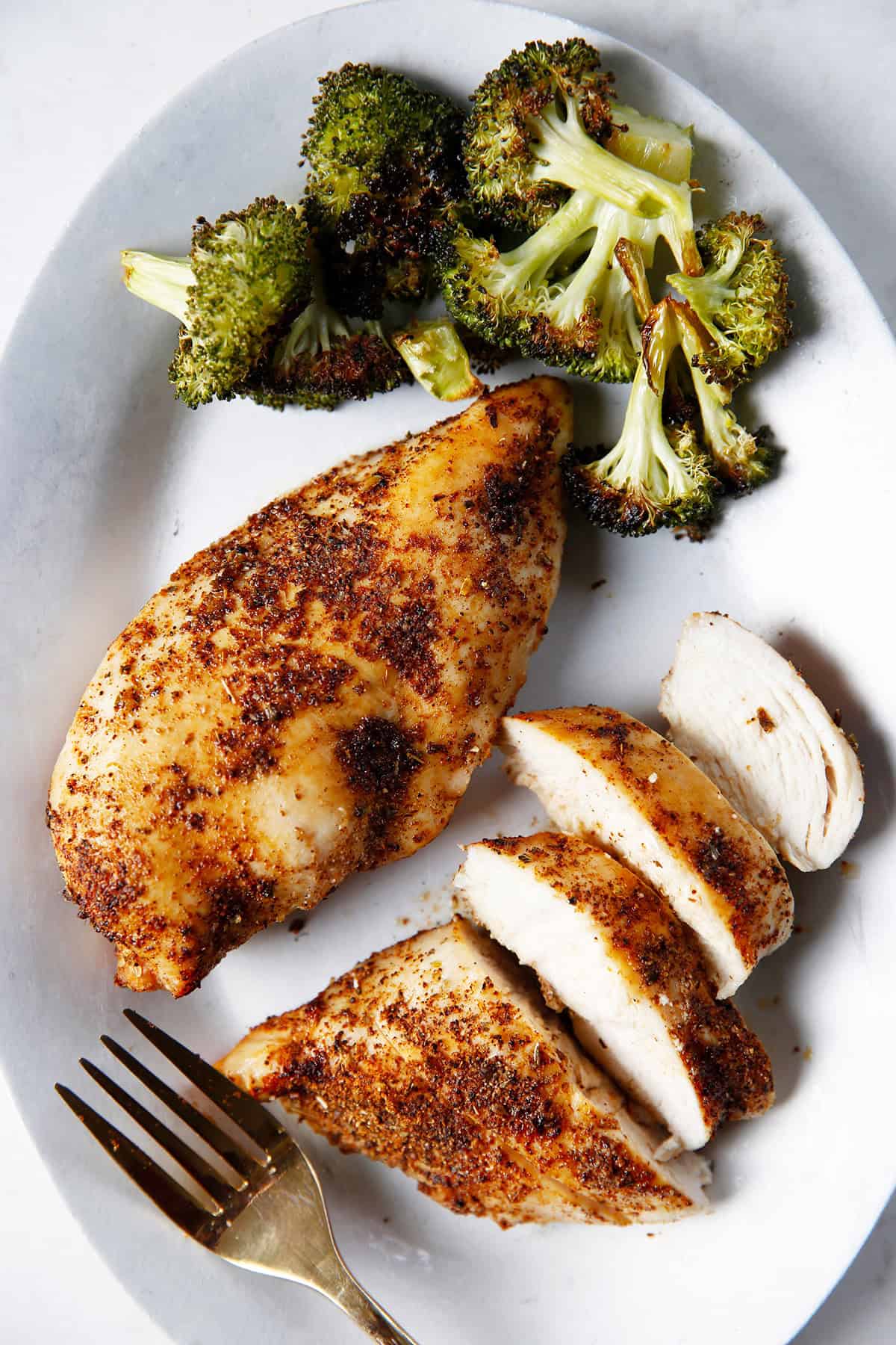 A plate with broccoli, a whole air fryer chicken breast, and chicken pieces.