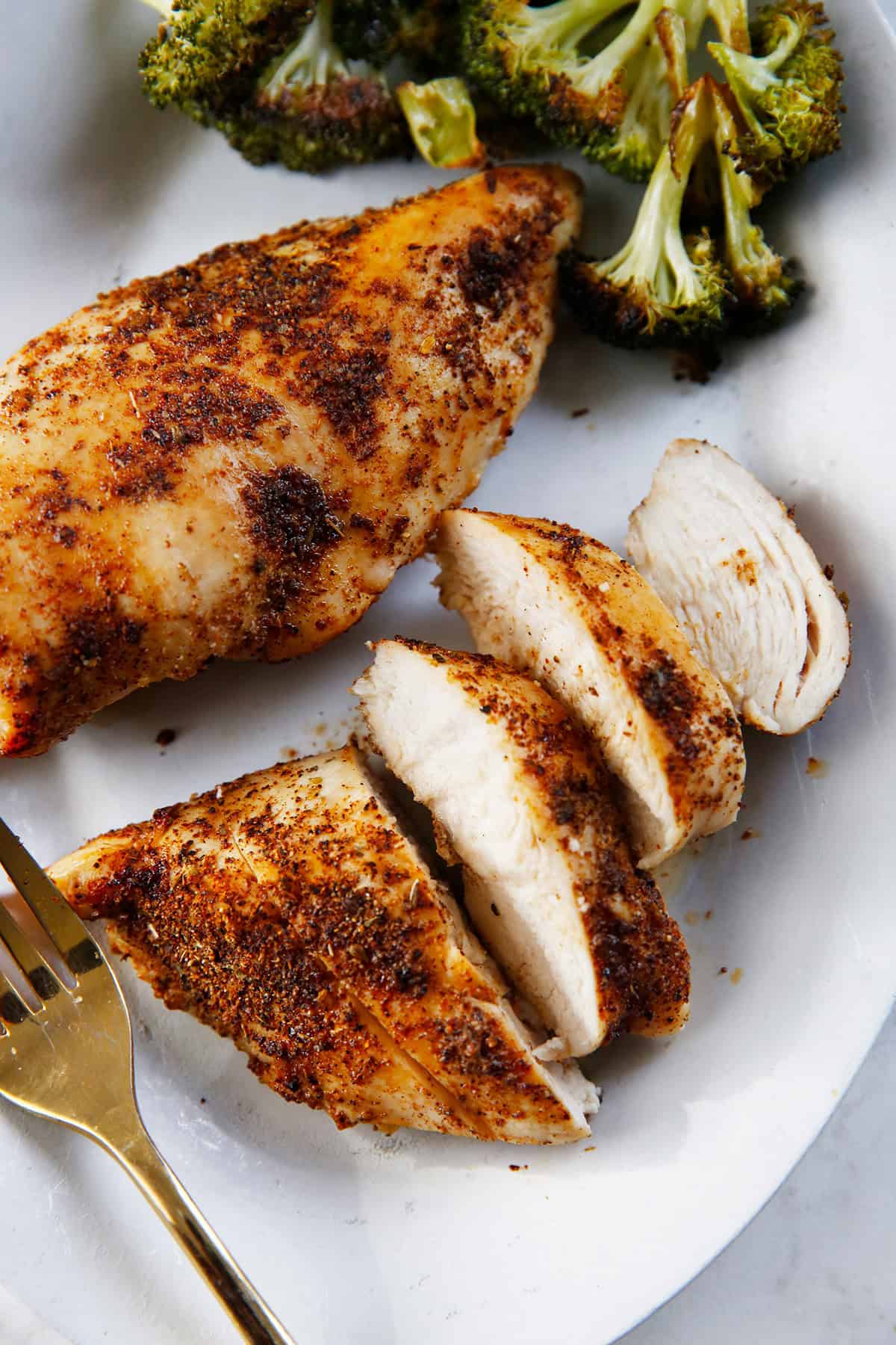 Sliced air fryer chicken breast on a plate with broccoli.