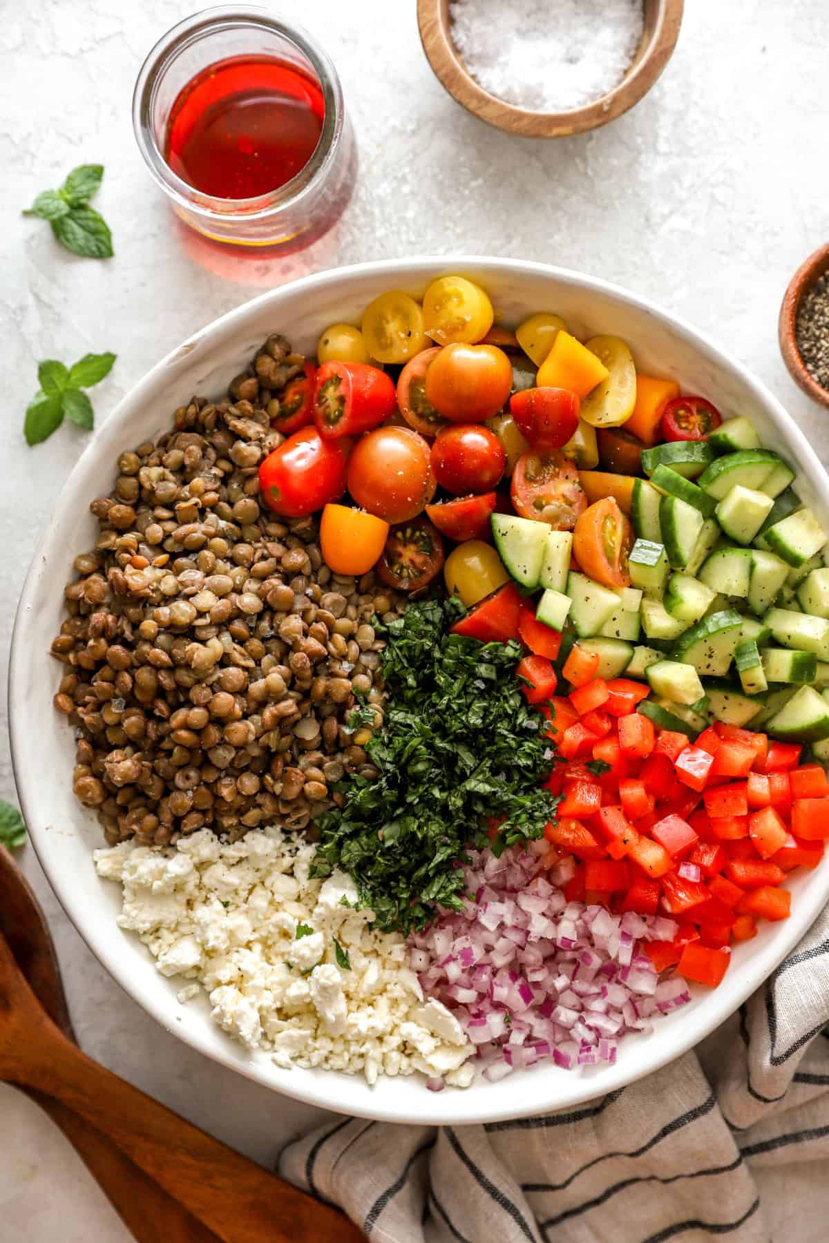 Lentils, tomatoes, cucumbers, peppers, red onions, feta, and herbs in a bowl. 