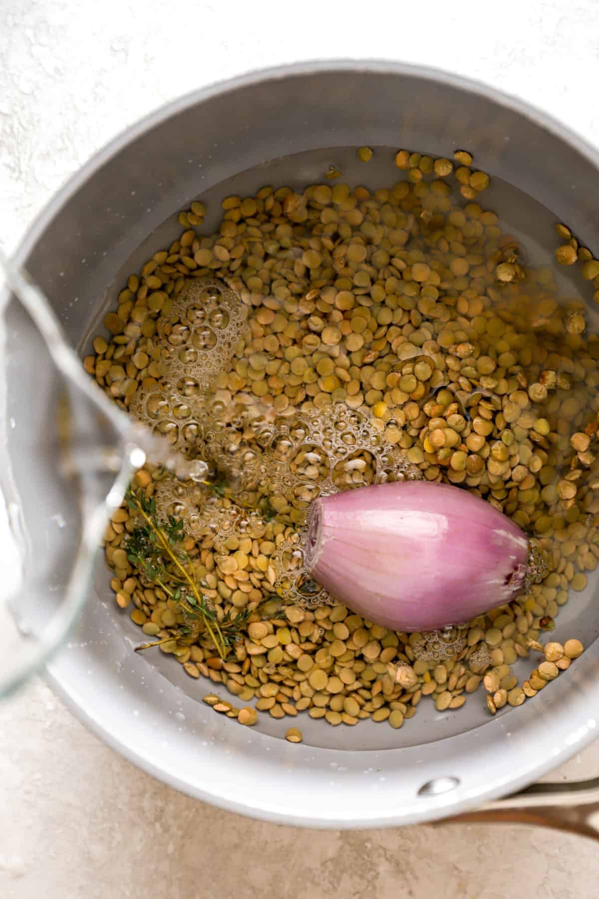 Water being poured over lentils and a shallot in a pot. 