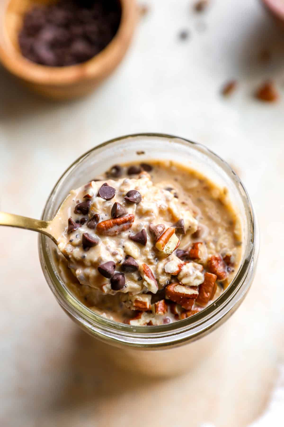 A spoon lifting a bite of pumpkin overnight oats from a jar. 