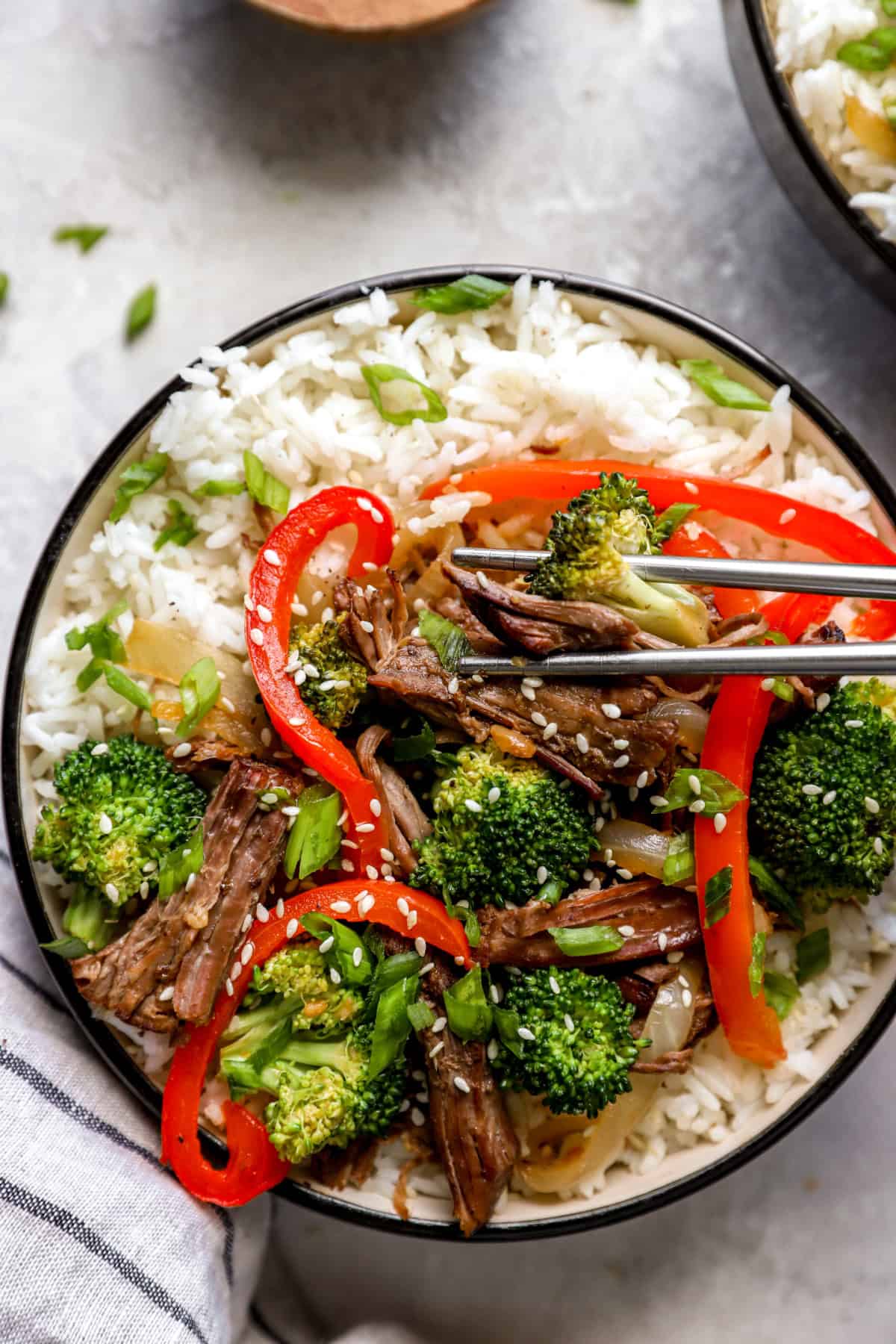 Chopsticks holding a piece of Paleo beef over a bowl of beef, veggies, and rice. 