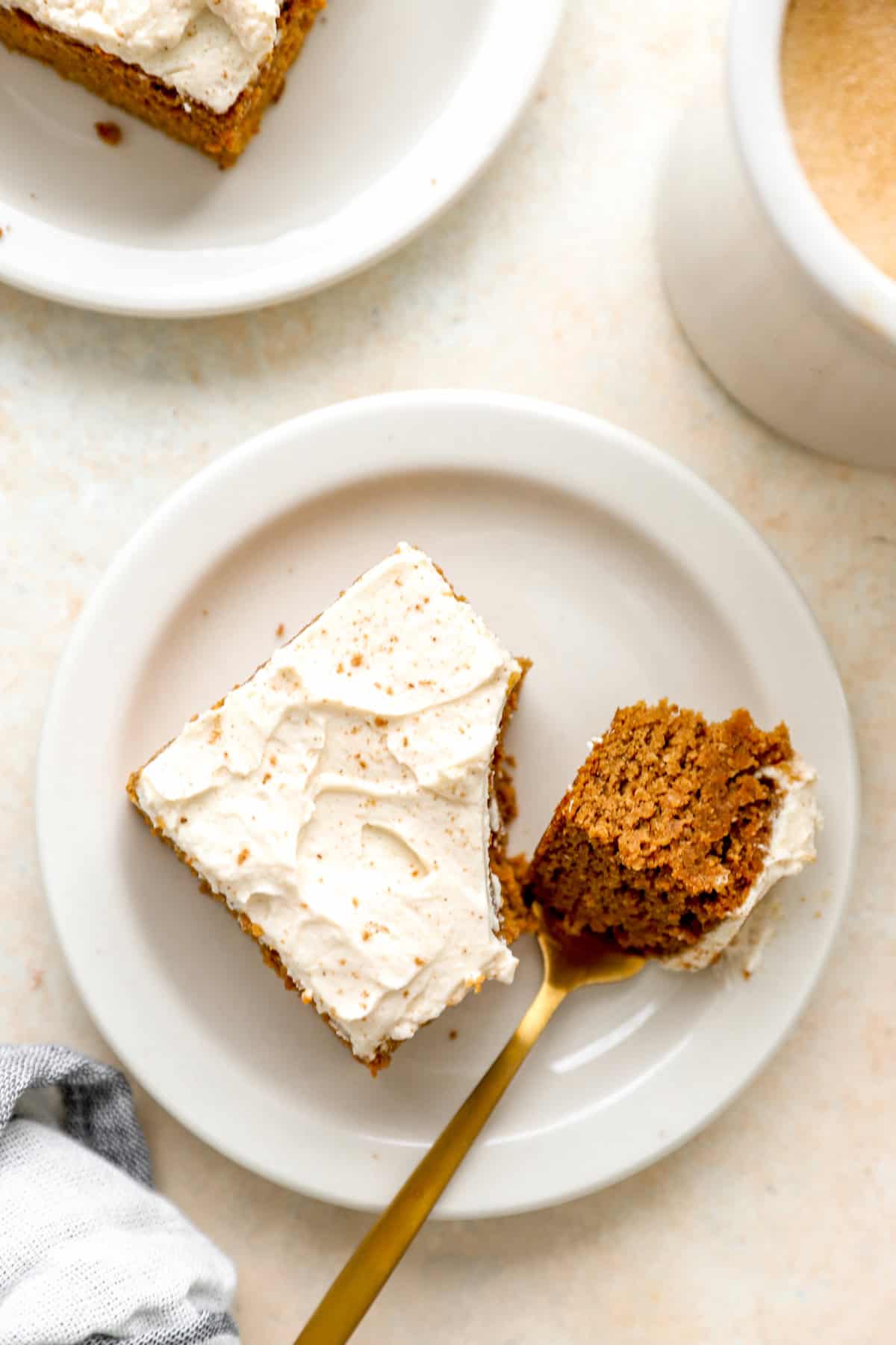 A fork holding a bite of gluten free pumpkin cake on a plate next to the slice of cake. 