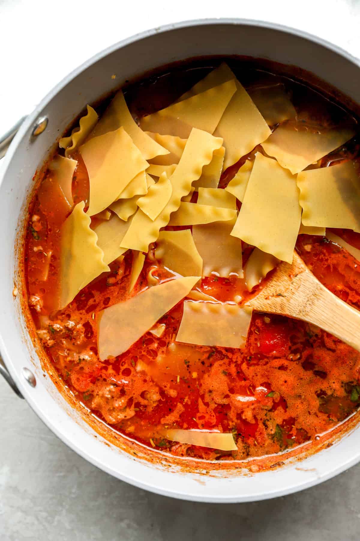 Lasagna noodles being stirred into a pot of soup.