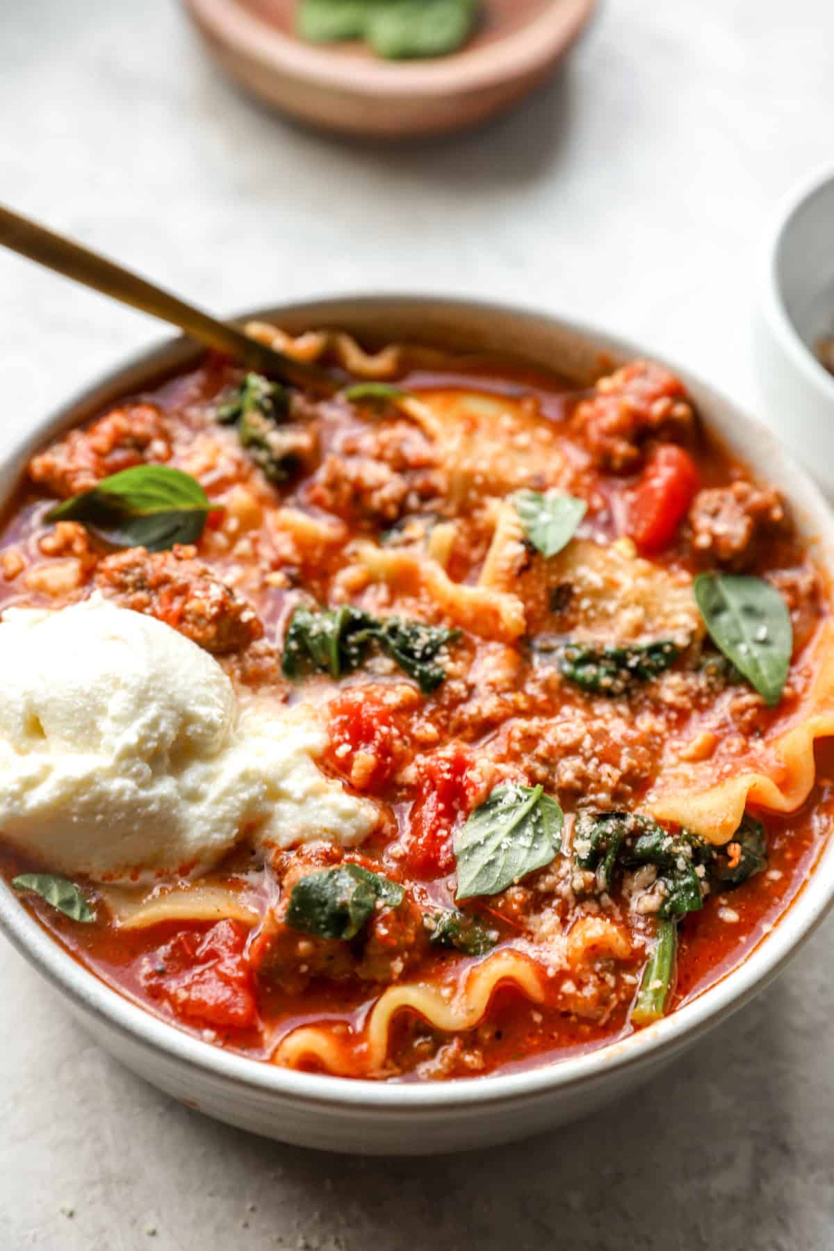 A bowl of lasagna soup topped with cheese. 