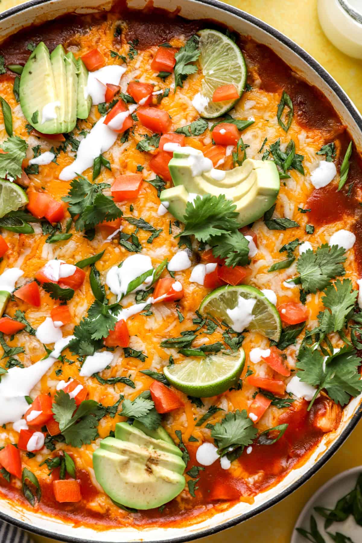 Overhead image of a baked skillet enchiladas dish topped with lime, avocado, cilantro, and sour cream. 