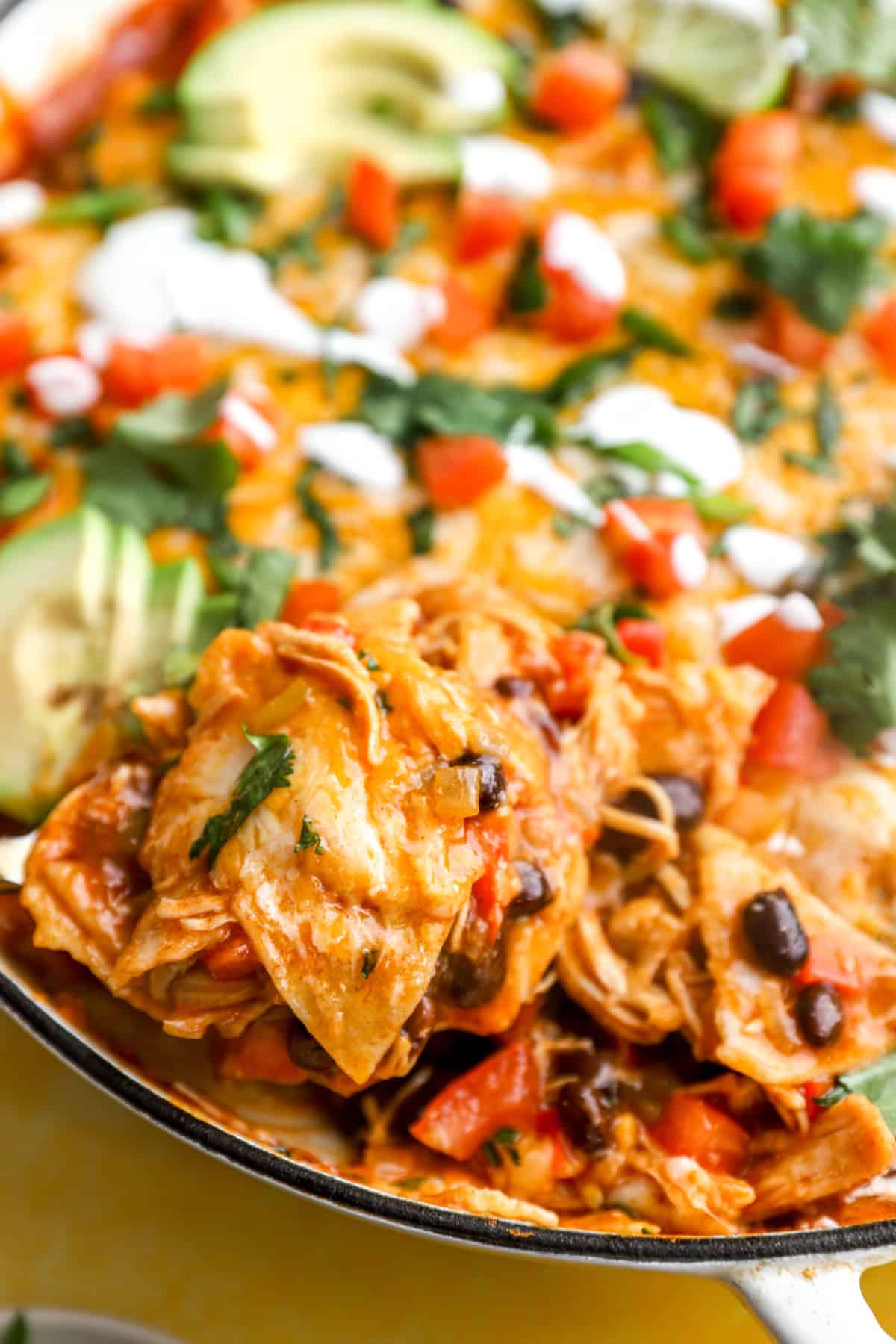 A spoonful of chicken skillet enchiladas being lifted from a skillet. 