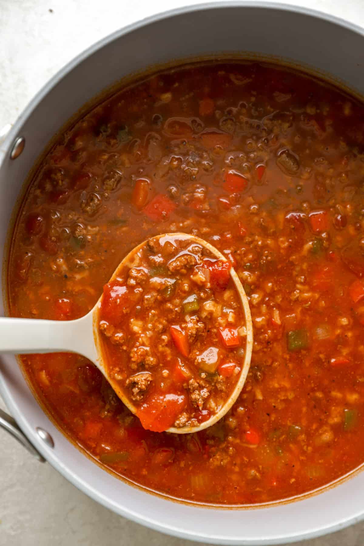 A spoon lifting a ladle of lasagna soup from a slow cooker. 