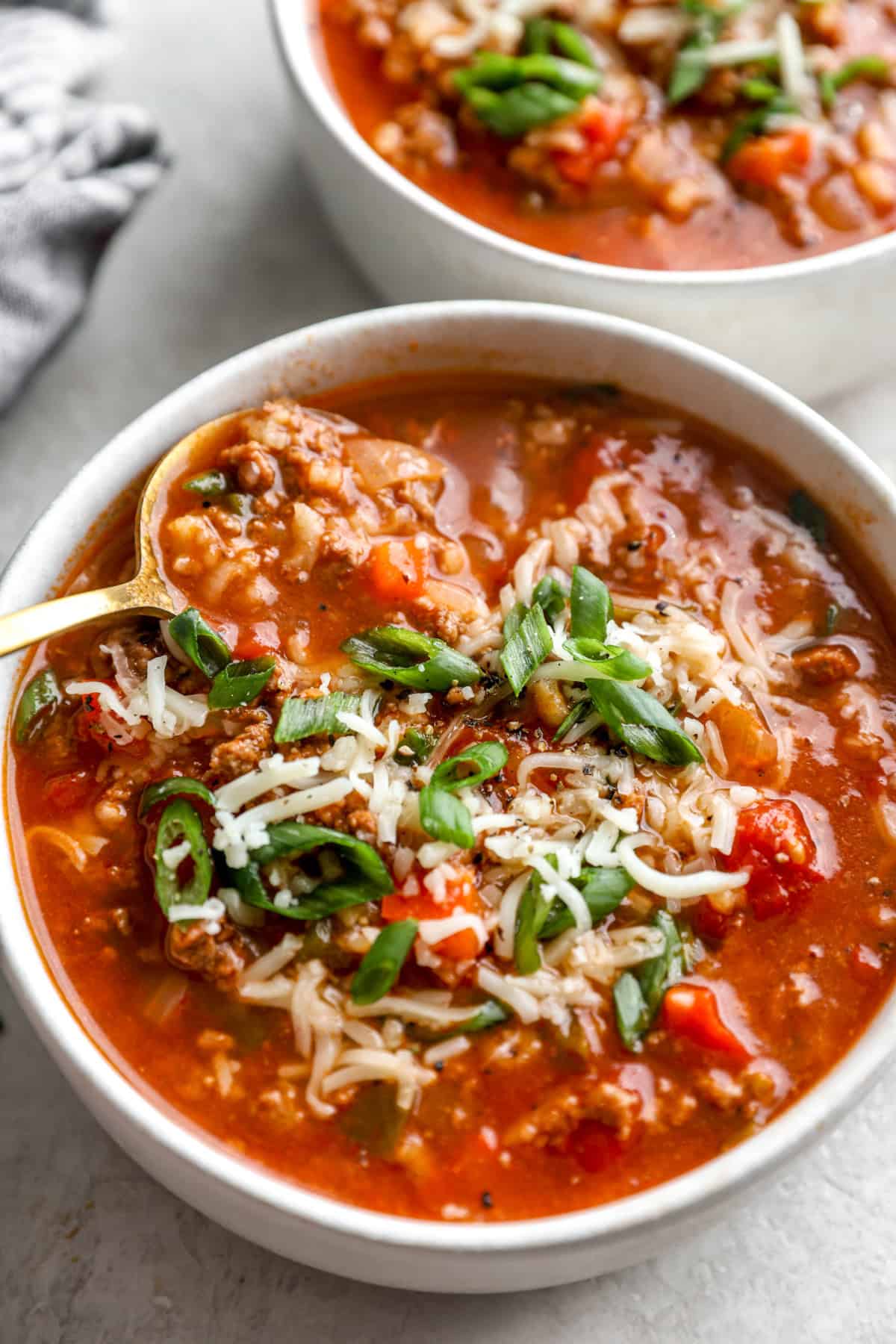 A spoon holding a scoop of soup on top of a bowl of stuffed pepper soup. 