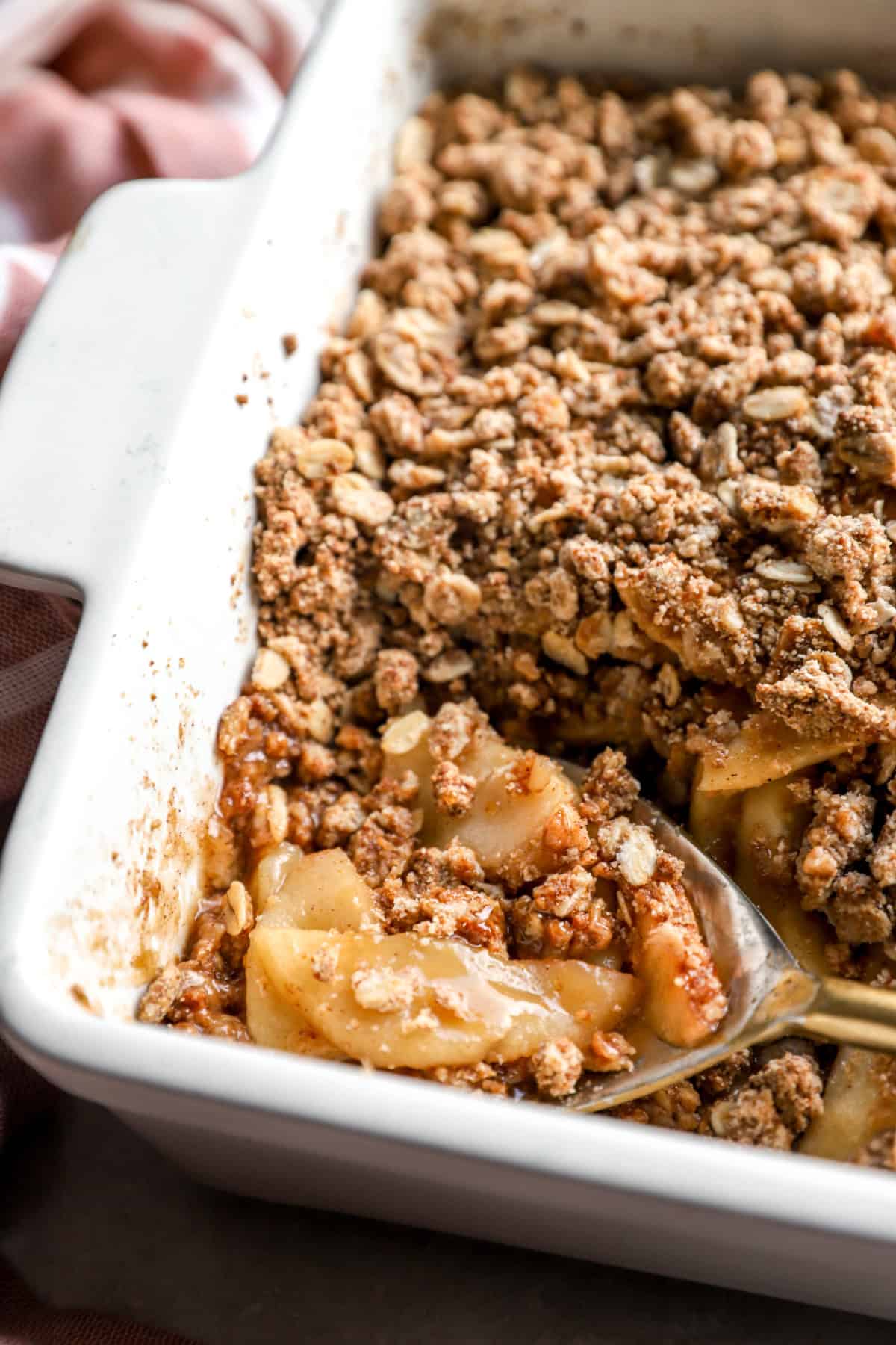 A spoon lifting a scoop of apple crisp from a pan. 