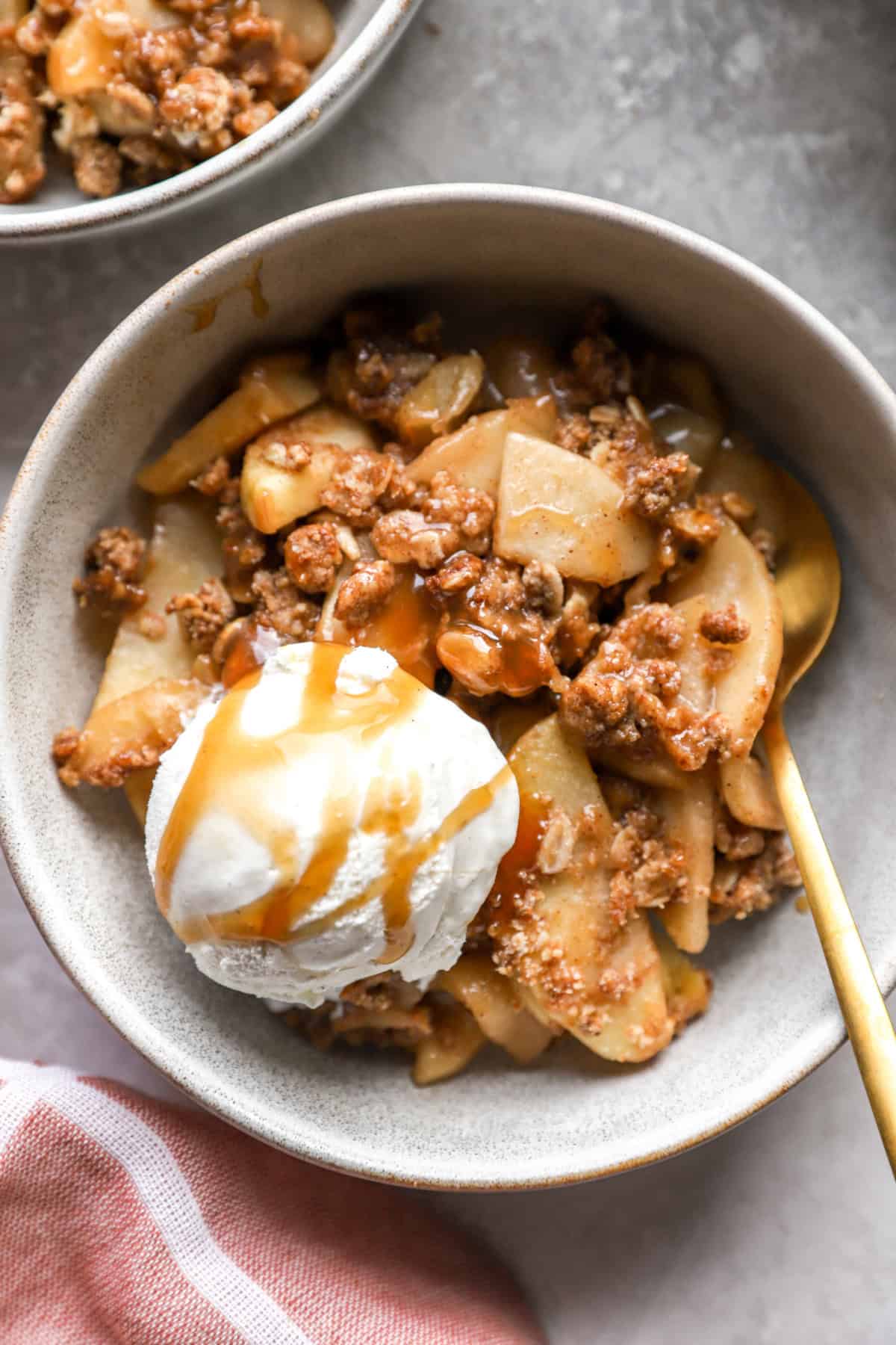 A bowl of apple crisp topped with ice cream and caramel. 