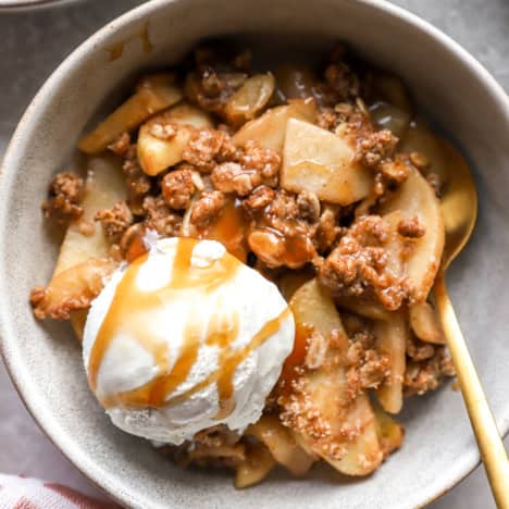 A bowl of apple crisp topped with ice cream and caramel.