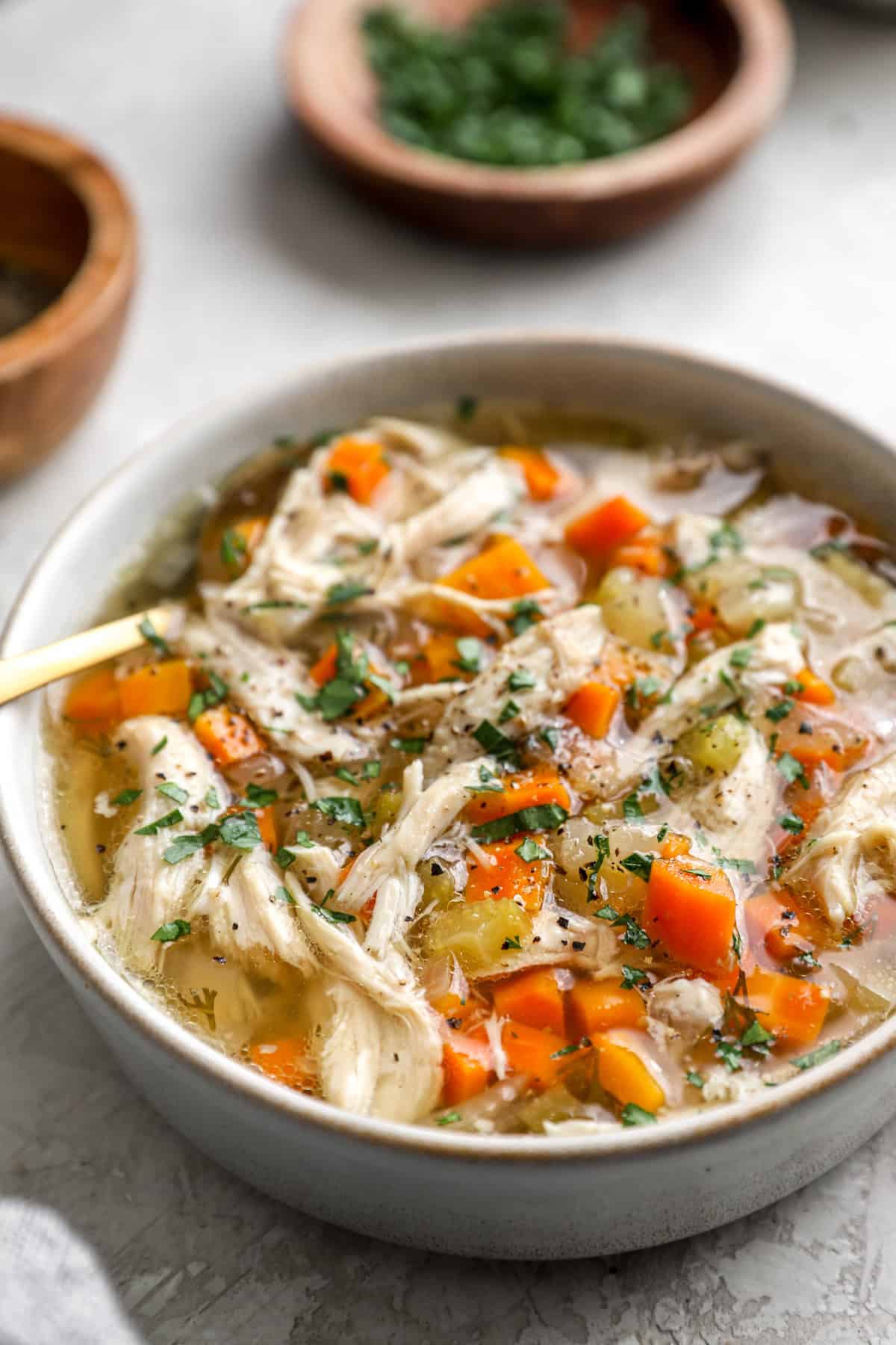 A bowl of slow cooker chicken soup with a spoon sticking out. 