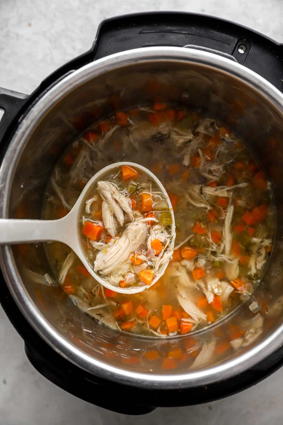 A ladle lifting a scoop of chicken soup from an Instant Pot.