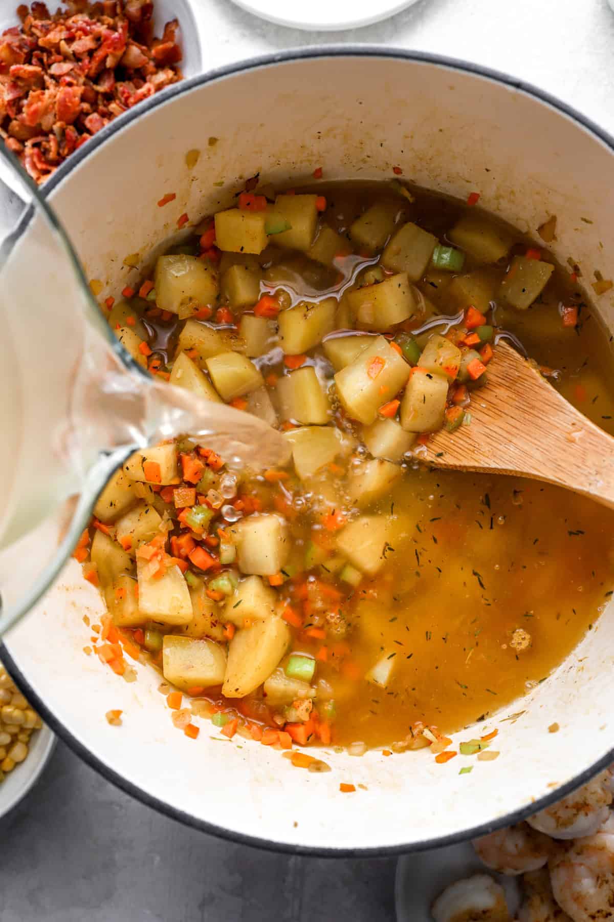 Ingredients for creamy potato shrimp and corn chowder being added to a pot.