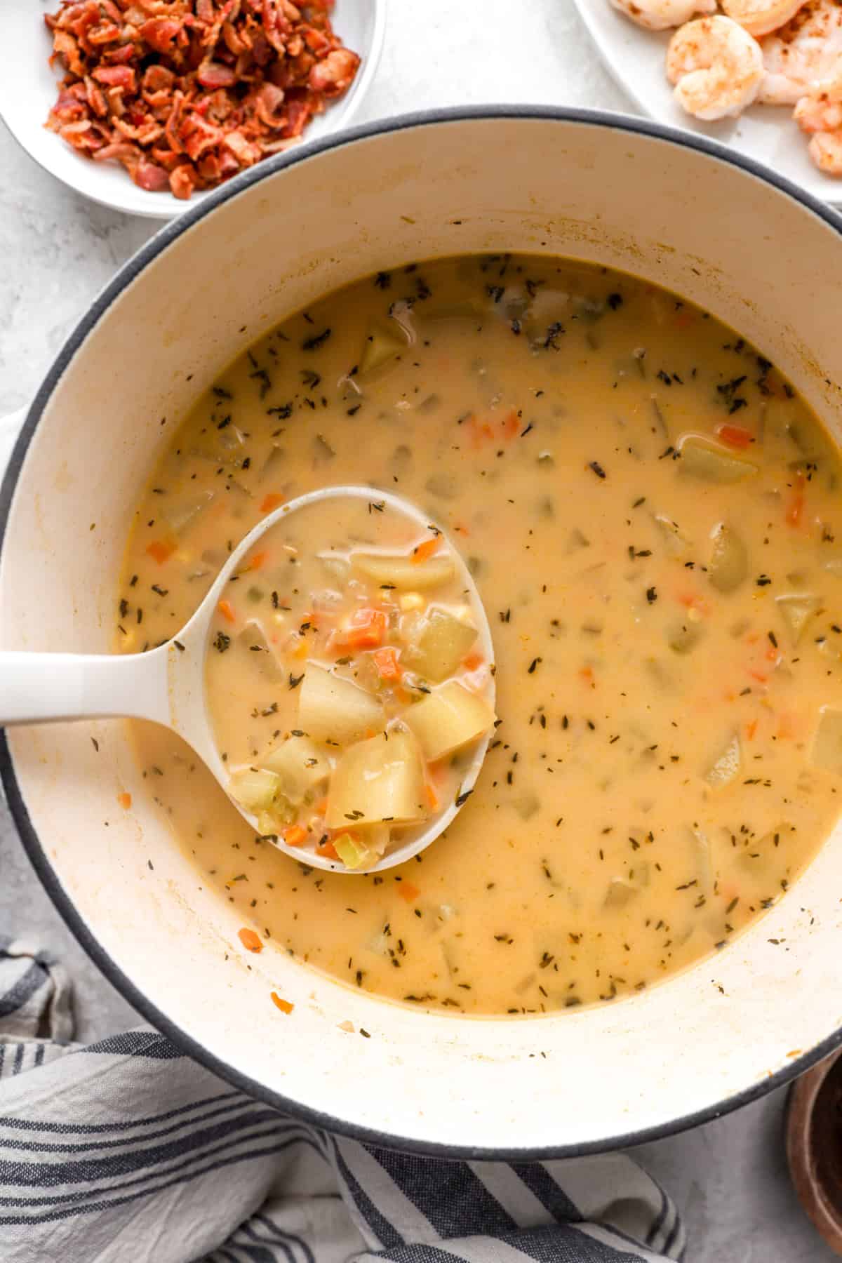 A ladle lifting a scoop of potato shrimp and corn chowder from a pot.