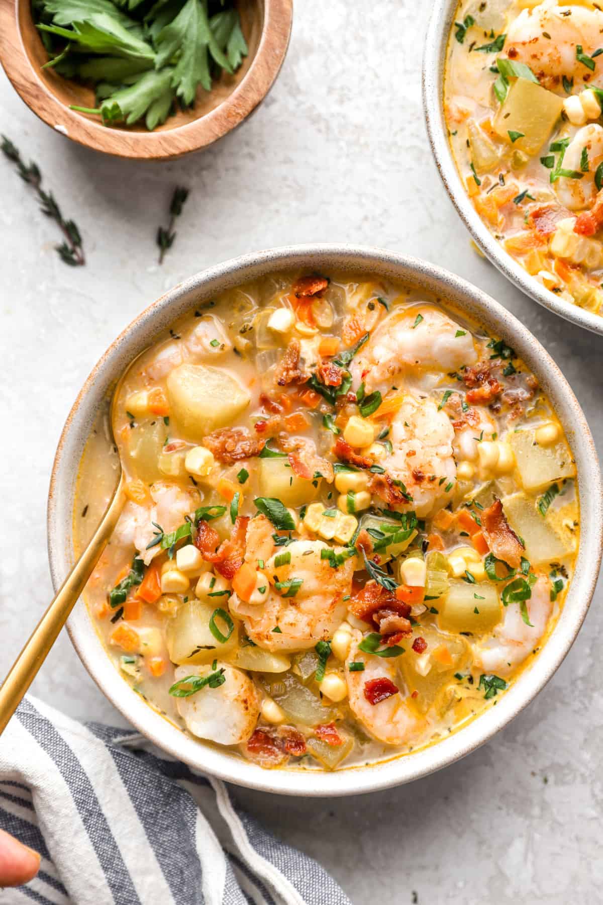 A bowl of bacon, potato, shrimp, and corn chowder with a spoon sticking out. 