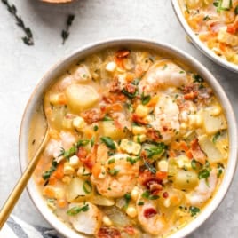 A bowl of bacon, potato, shrimp, and corn chowder with a spoon sticking out.