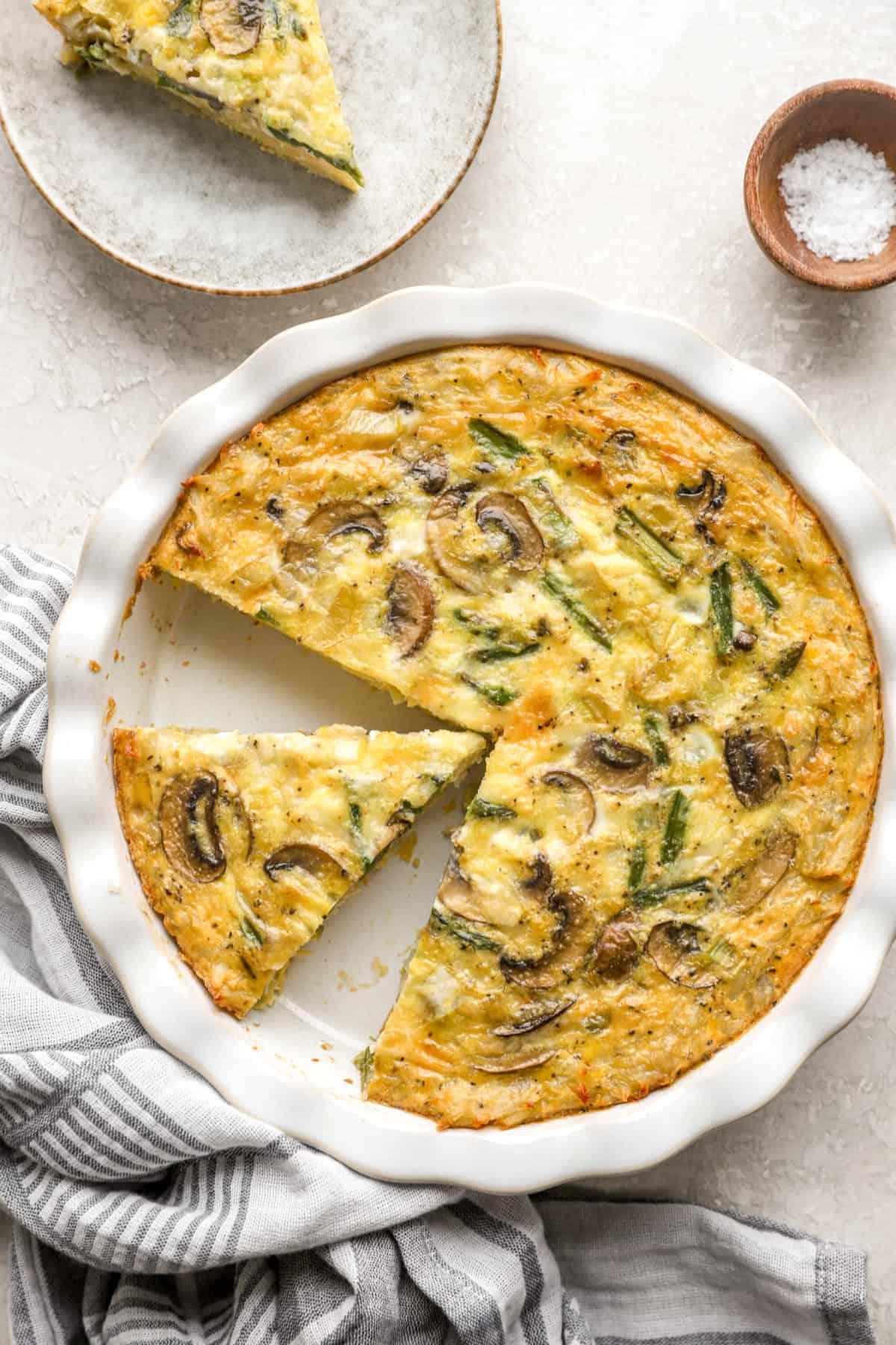 Overhead image of a hash brown crust quiche with a slice cut. 