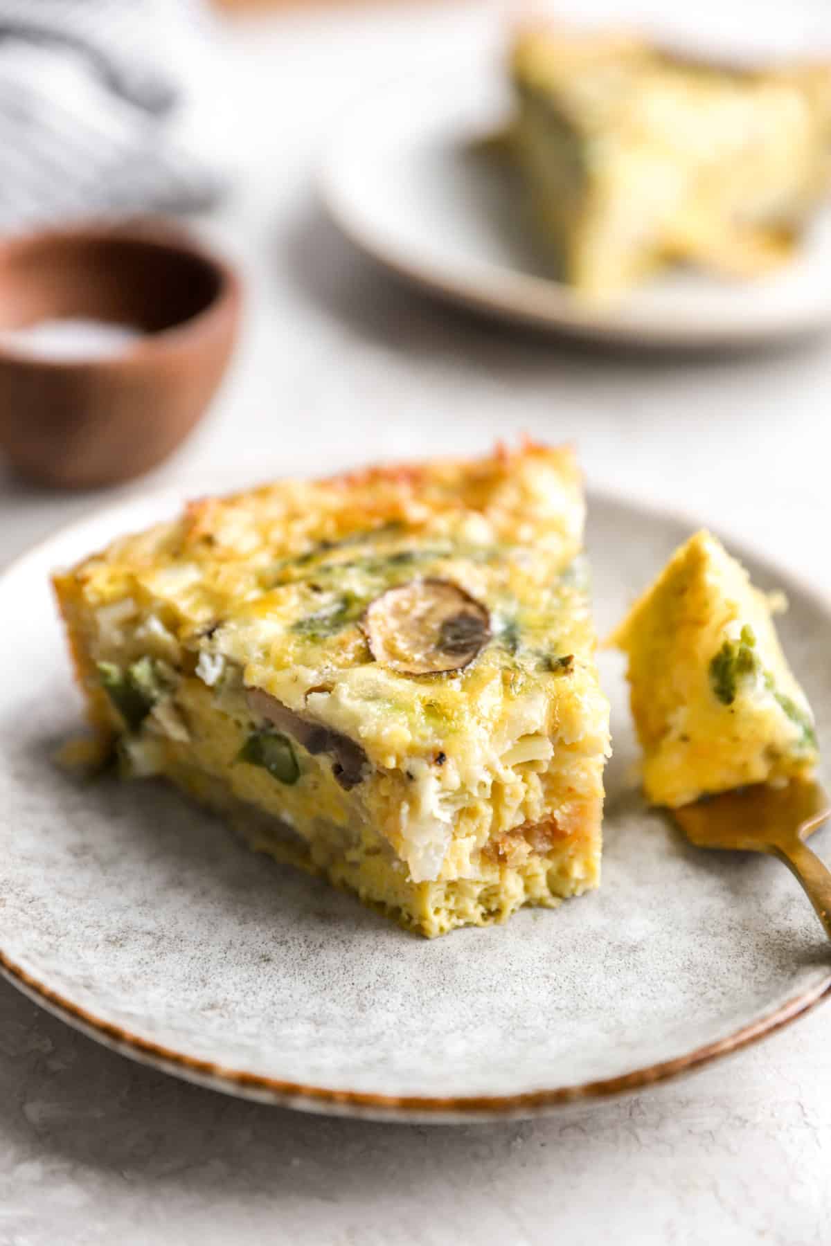 A slice of hash brown crust quiche on a plate with a fork holding a bite. 