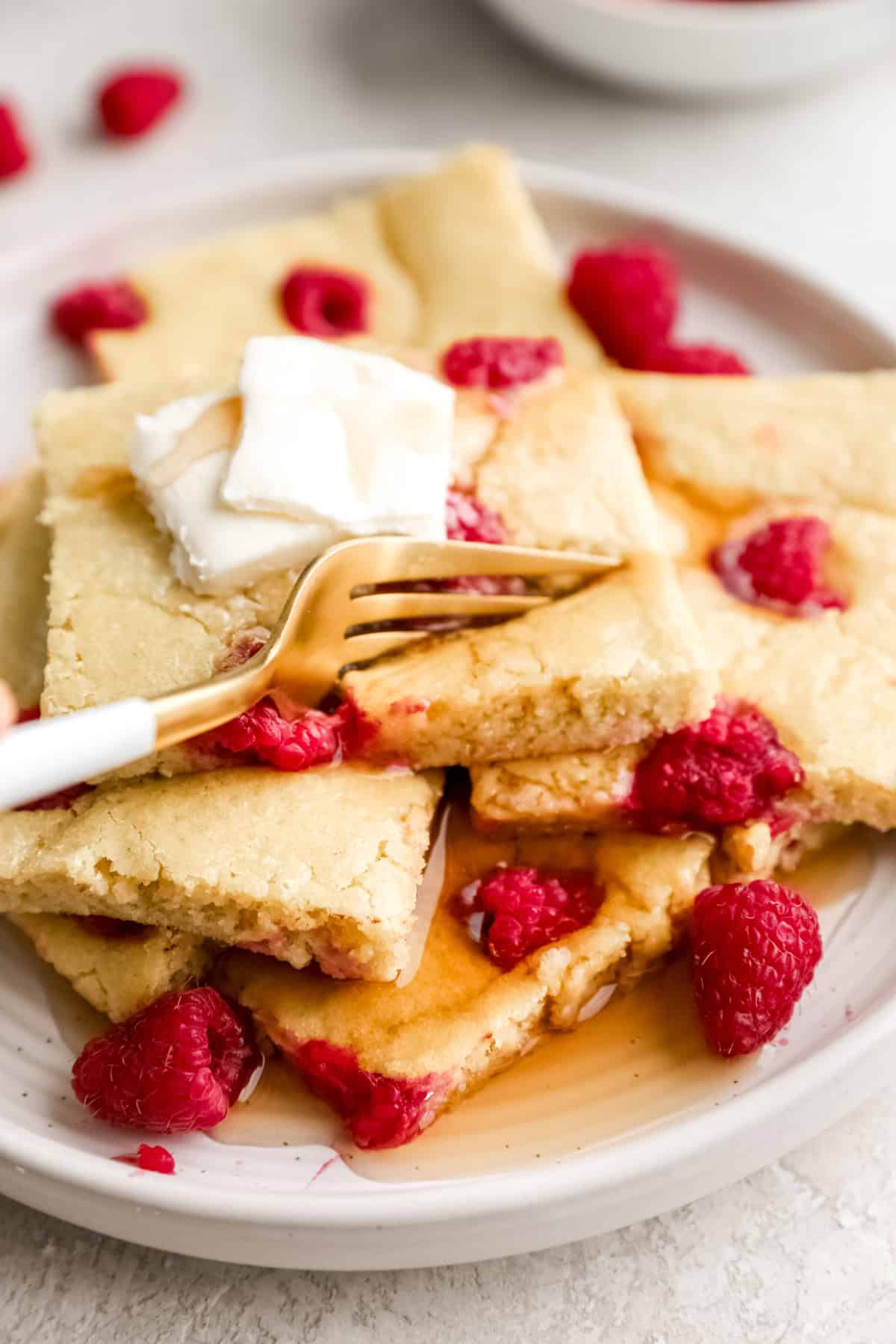 A plate of sheet pan pancakes topped with butter and raspberries. 