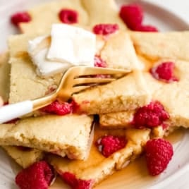 A plate of sheet pan pancakes topped with butter and raspberries.