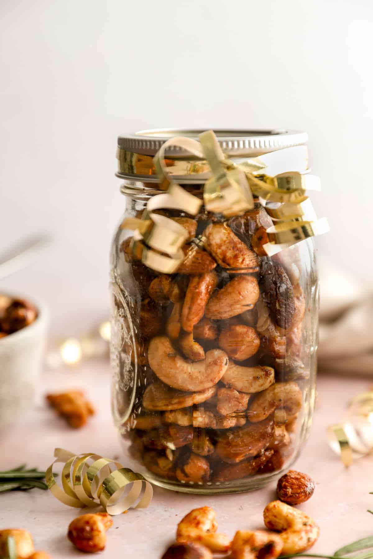 A mason jar of party nuts wrapped with golden ribbon. 