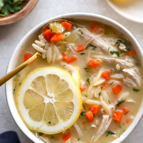 A bowl of avgolemono soup topped with a lemon slice.