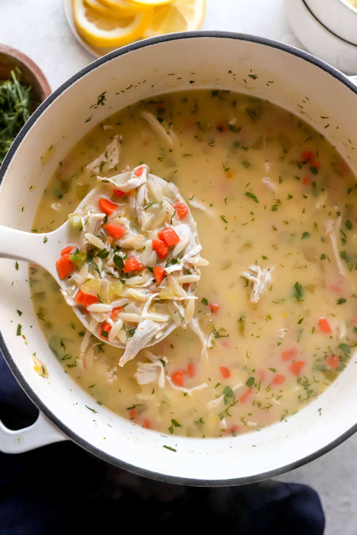 A scoop of Greek avgolemono soup being lifted from a pot. 