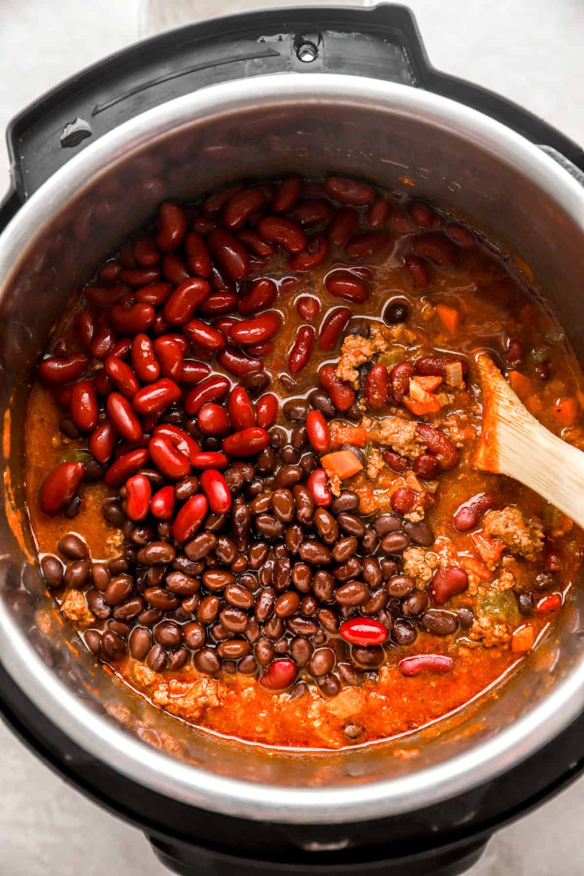 Beans being stirred into a beef chili recipe in an Instant Pot. 