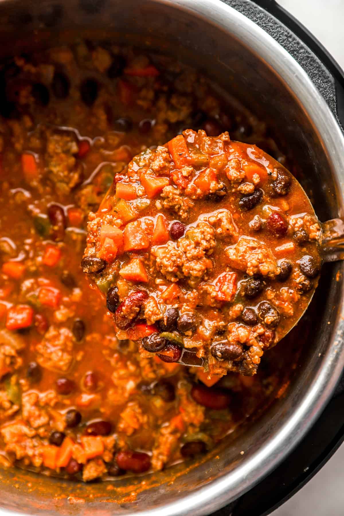 A ladle lifting a scoop of classic beef chili from an Instant Pot. 