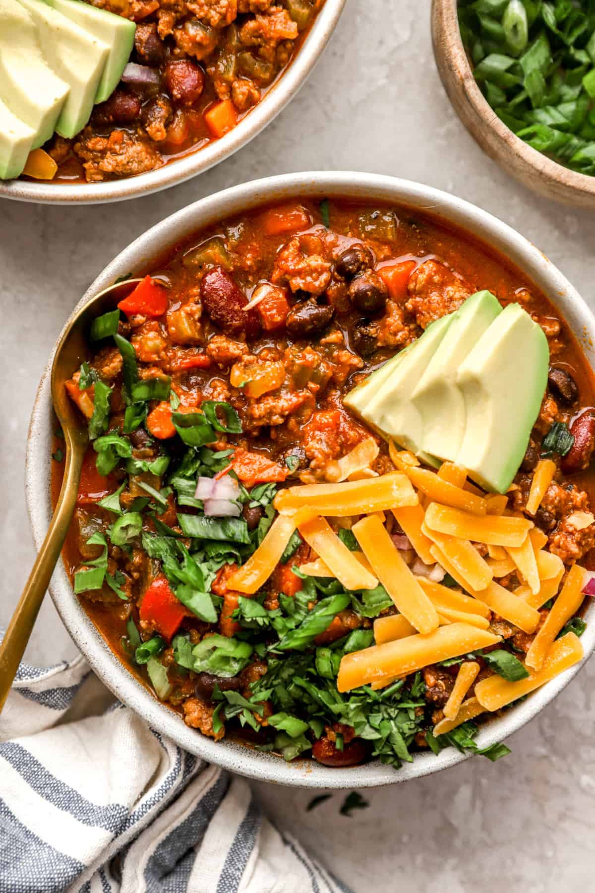 A bowl of a classic beef chili recipe topped with avocado, cheese, and cilantro. 