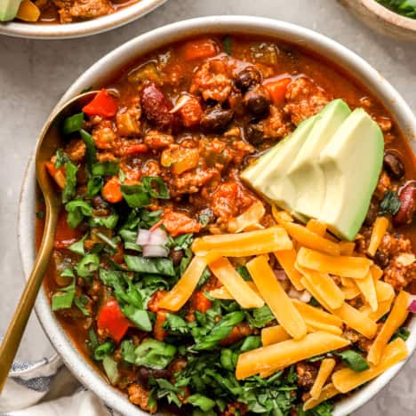 A bowl of a classic beef chili recipe topped with avocado, cheese, and cilantro.