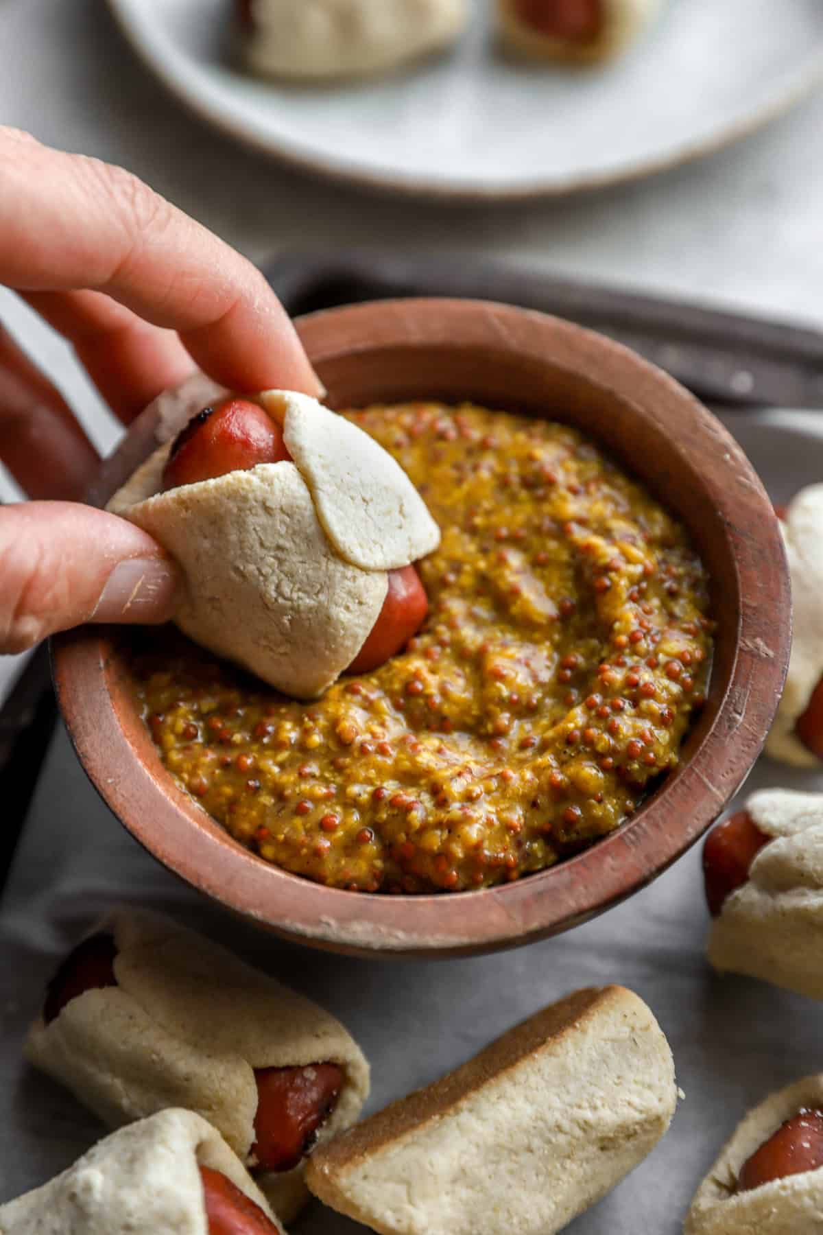 A hand dipping a gluten free pig in a blanket in sauce. 