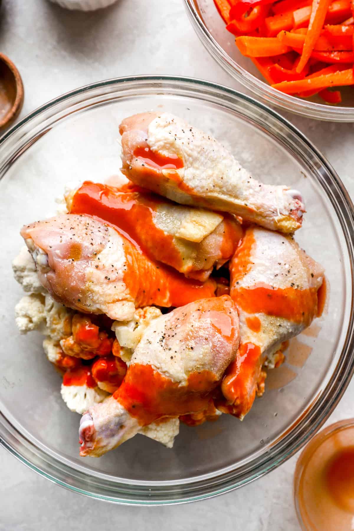 Raw chicken drumsticks being coated with buffalo sauce.