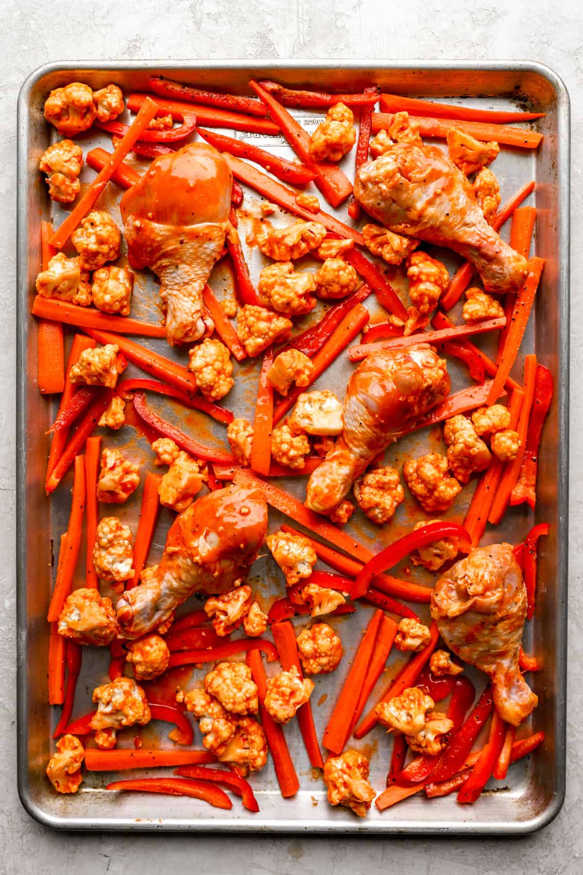 Buffalo chicken and veggies on a baking sheet.